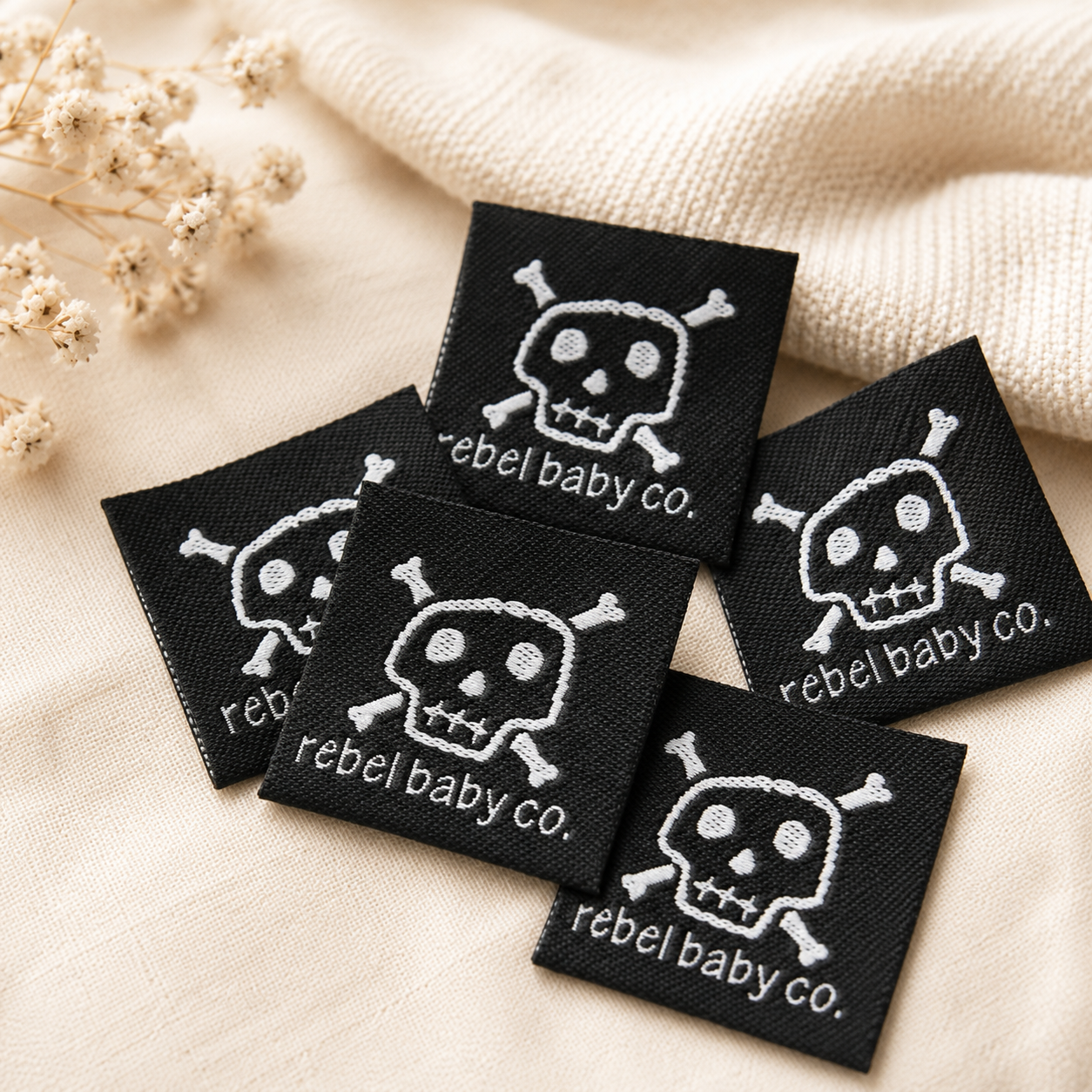 Black custom woven clothing labels with white skull logo on beige fabric