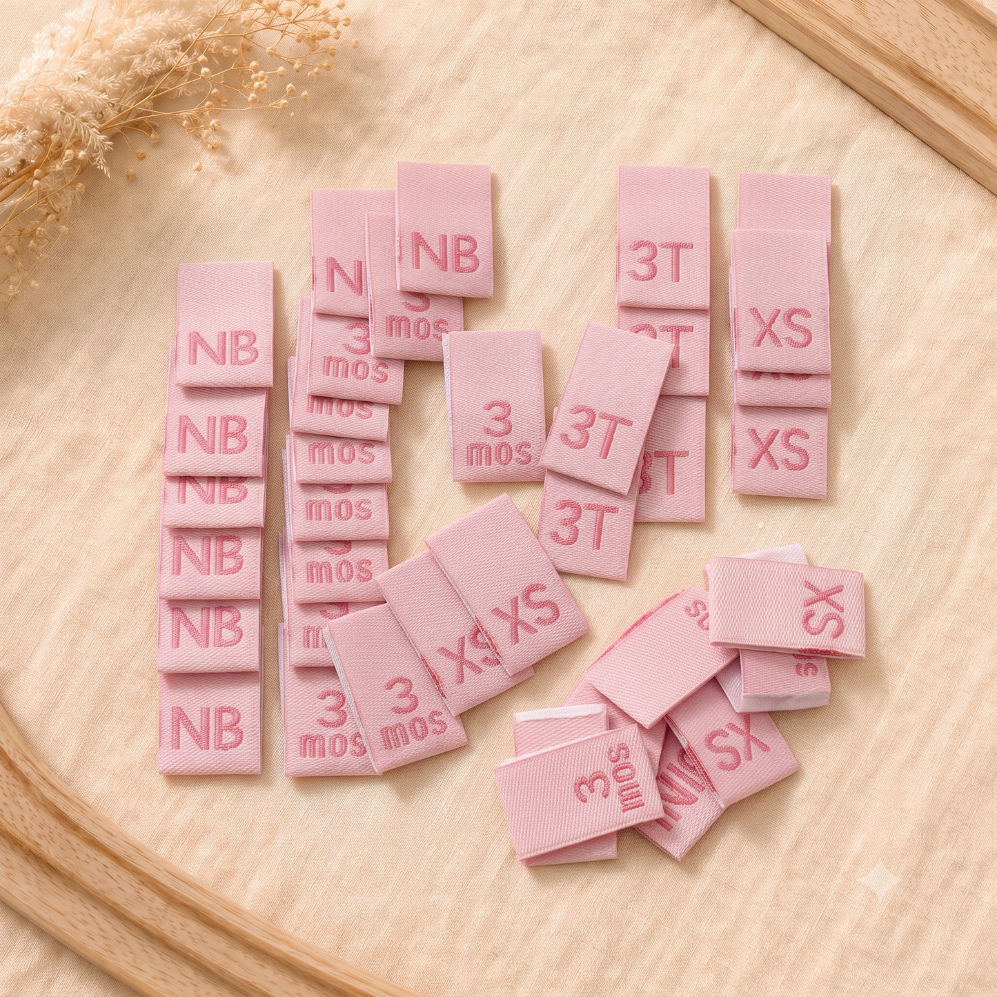 Pink woven baby size labels with NB, 3 mos, 3T and XS sizes for clothing and handmade garments