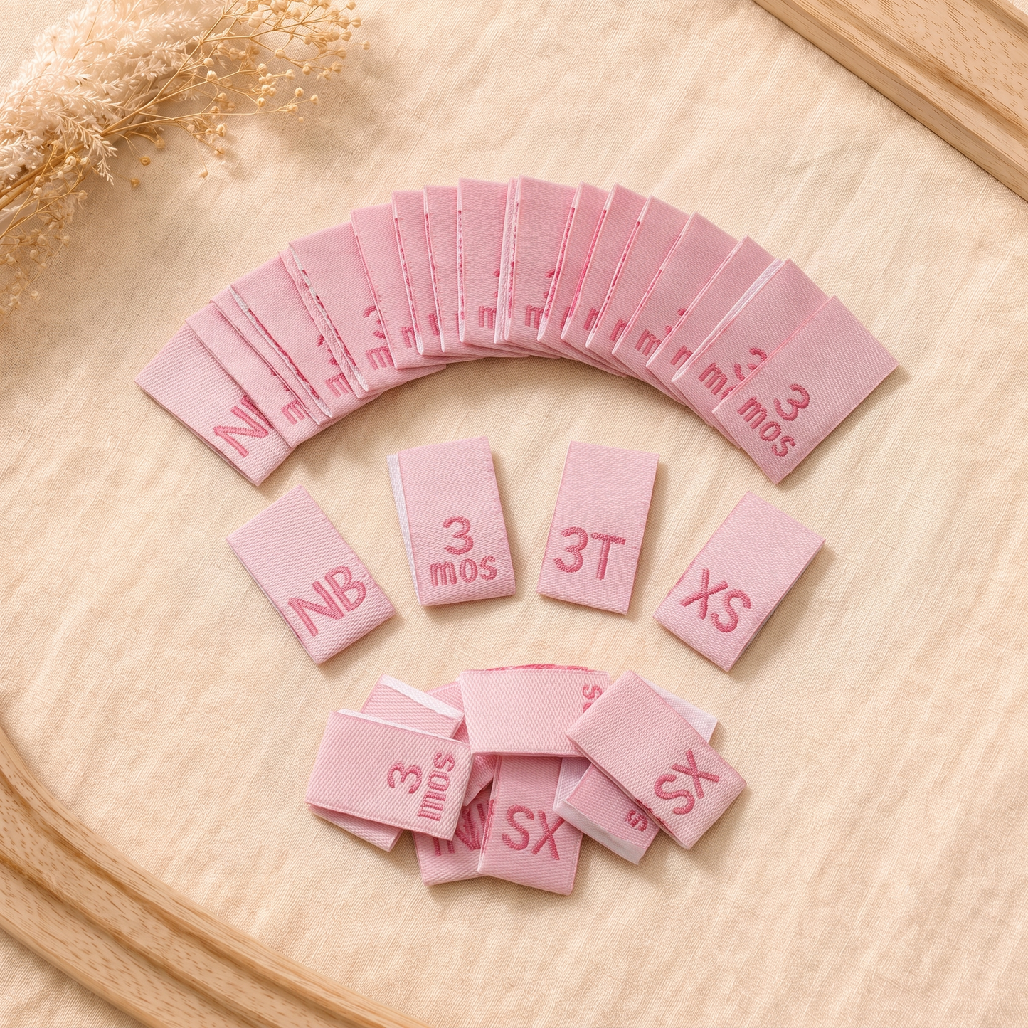 Pink woven baby size labels with NB, 3 mos, 3T and XS sizes for clothing and handmade garments